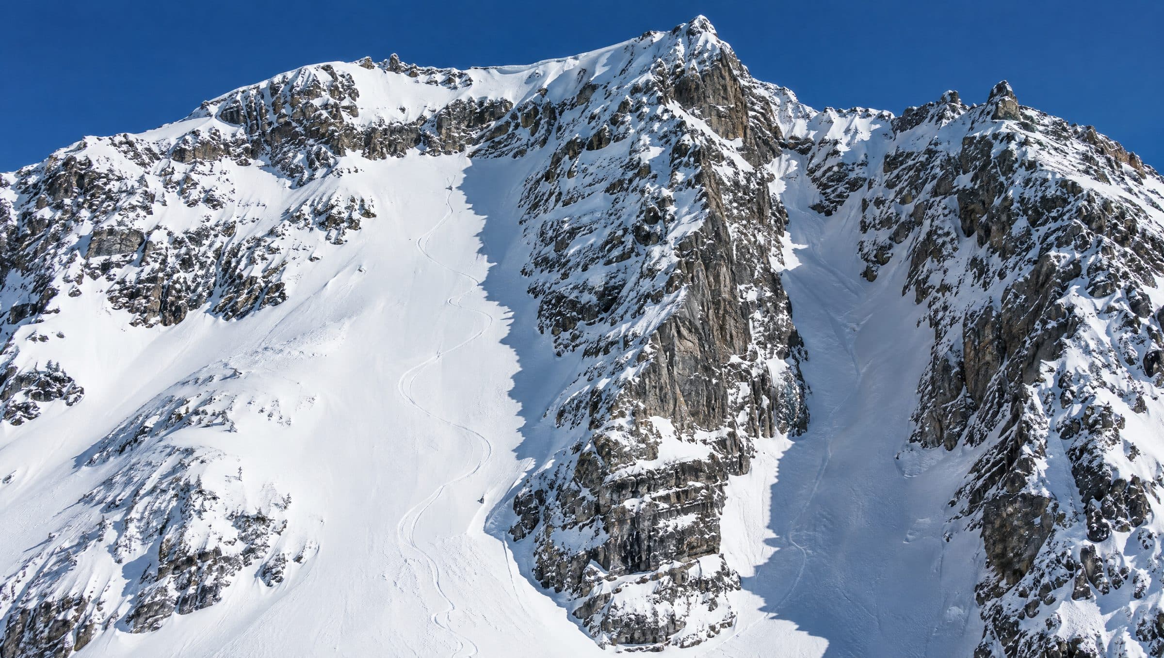 Steep alpine face in winter with rock bands, a couloir and fresh ski tracks