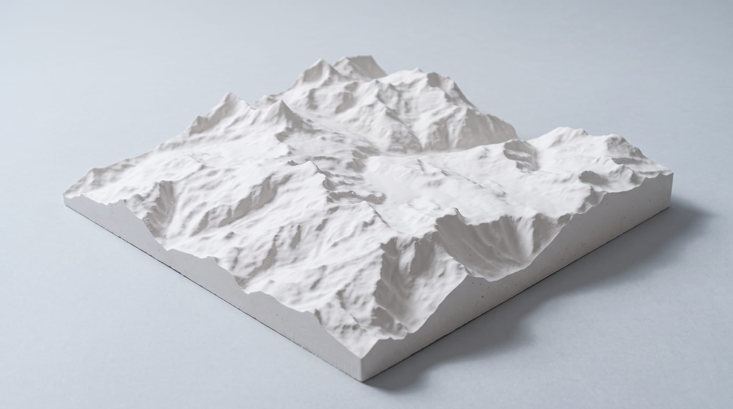 White plaster relief model of alpine terrain on a pale grey studio background